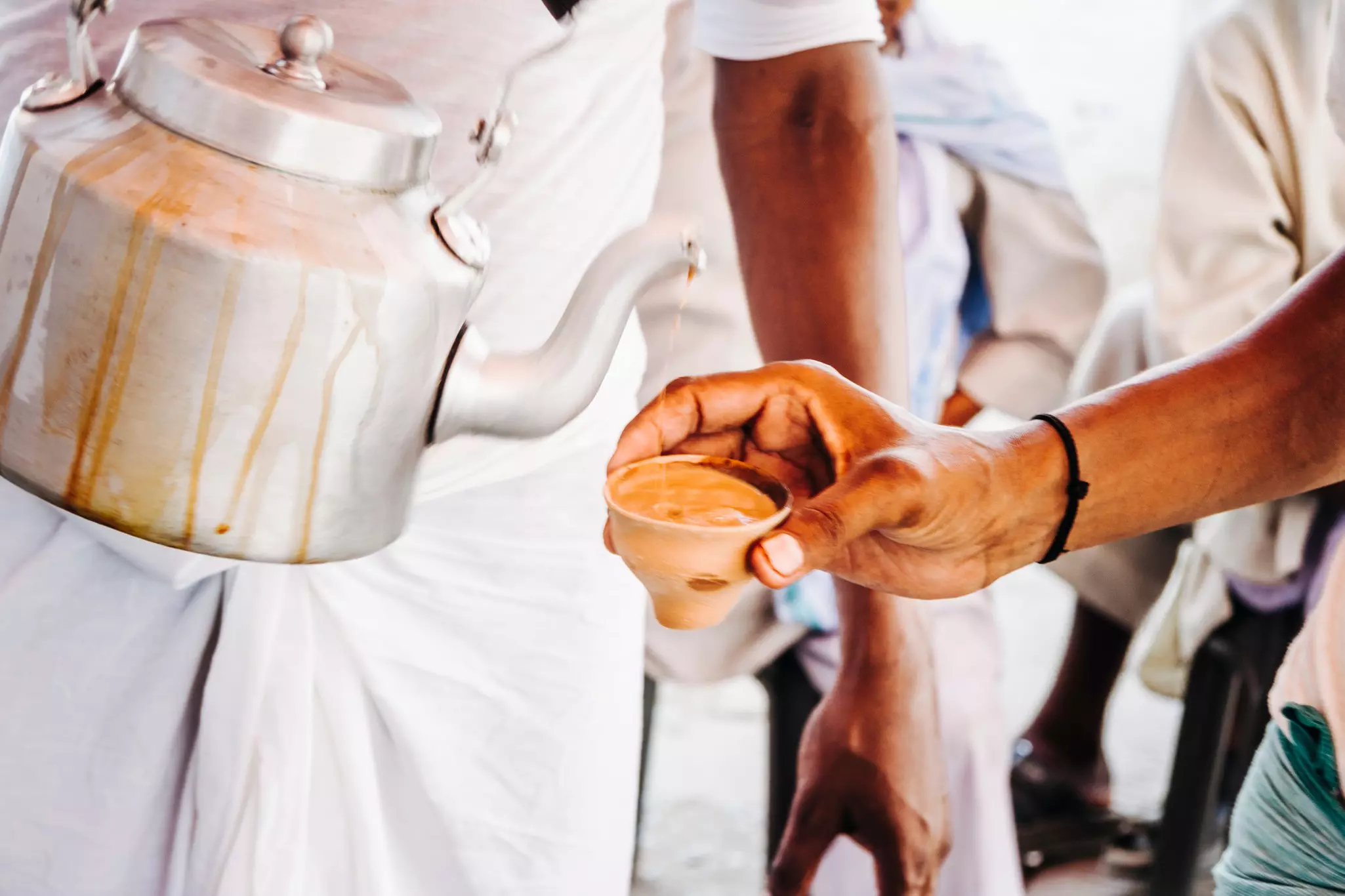 Tea is poured from a large silver kettle into a small handle-less clay pot.