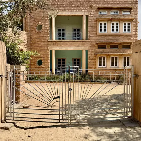 A tan stone building behind a gate has alcoves painted pale green.