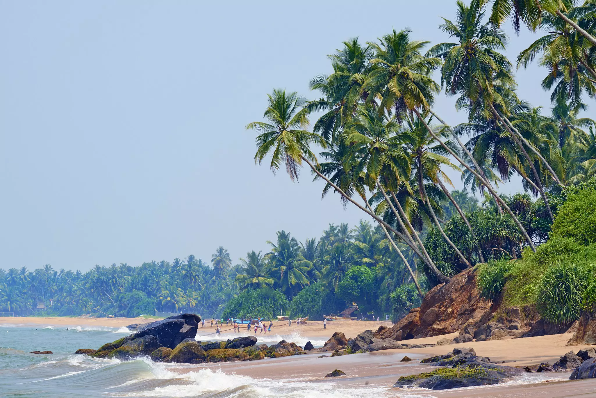 A beach with surf coming ashore by rocks in Sri Lanka.