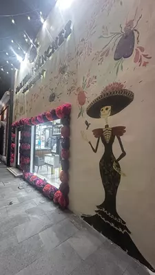 Sugar skull street art of a woman in a black dress and sombrero with pink flowers. 