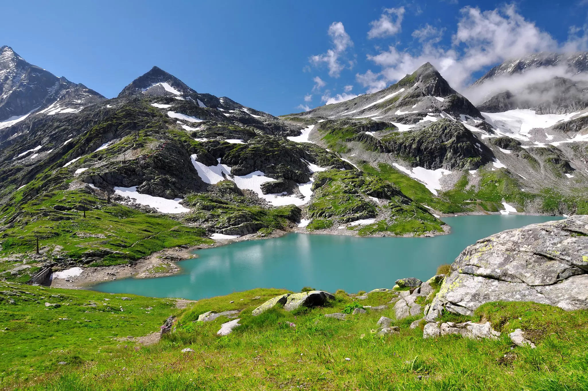 Lush mountains with bits of snow surround an azure lake.