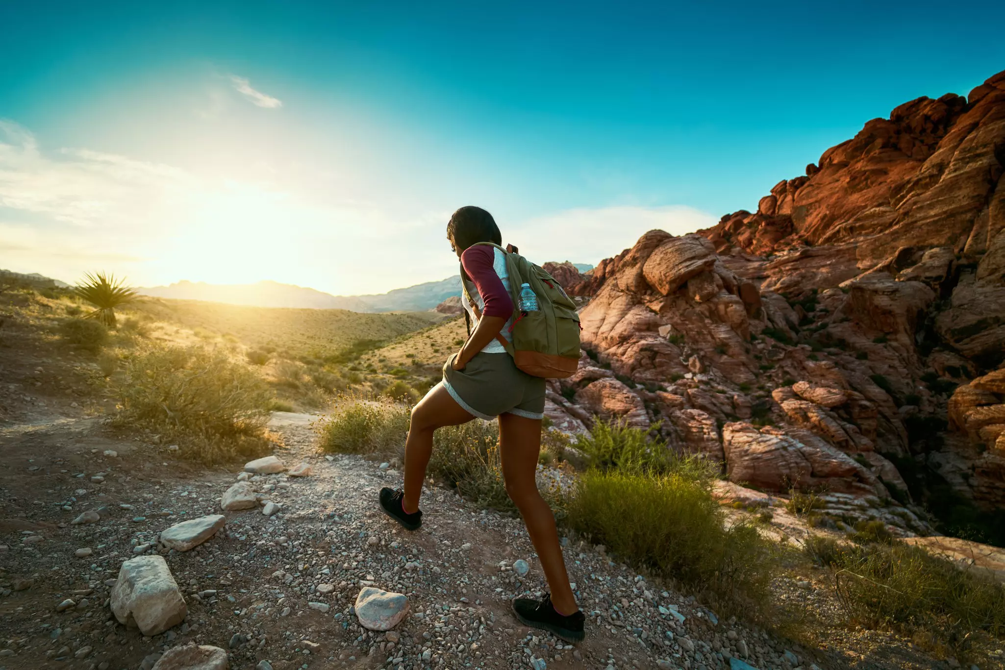 Woman with a backpack hiking on a rocky landscape at sunset