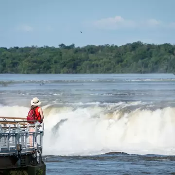 A person standing by a railing at a large waterfall.