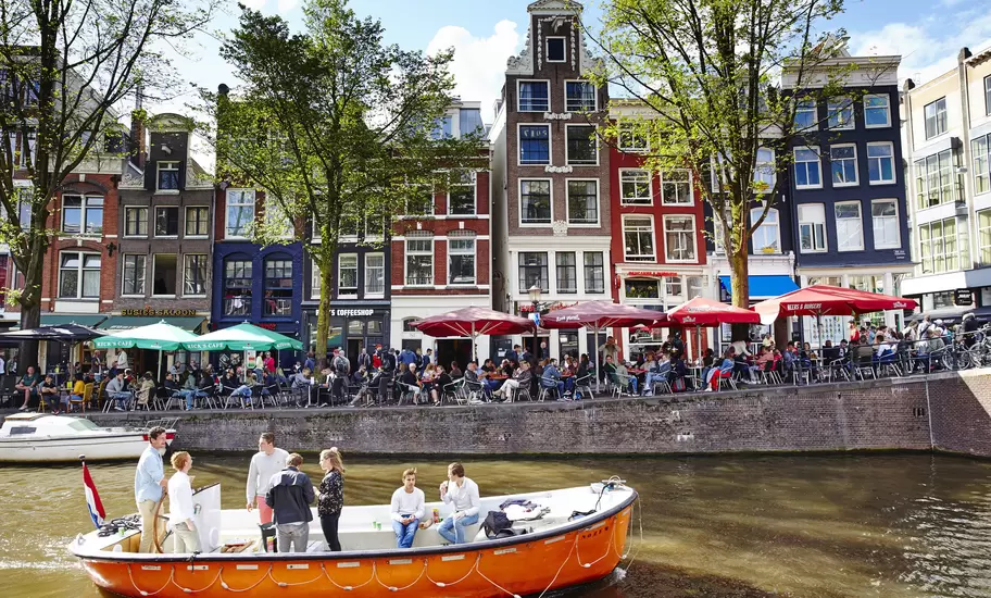 A boat travels down Oudezijds Voorburgwal, one of Amsterdam's oldest canals, with colorful houses in the background.