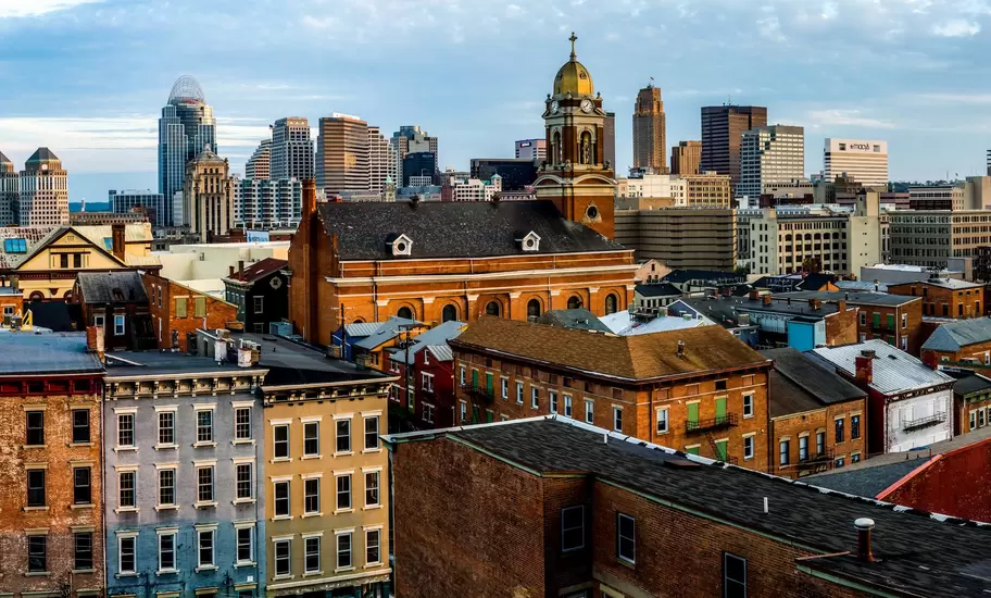 Brick row houses and a gold-domed church tower in Cincinnati's Over-the-Rhine, with downtown skyscrapers rising behind