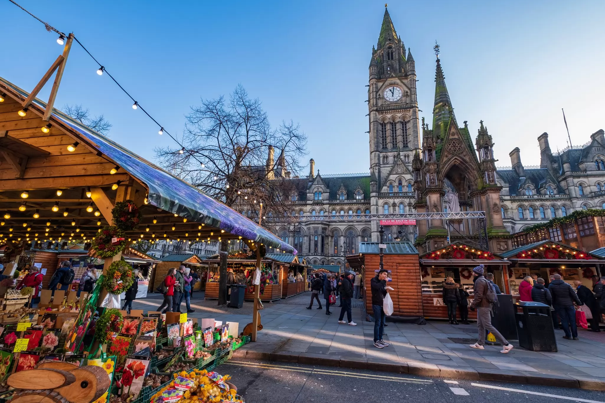 Festive wooden stalls selling Christmas gear set up in the shadow of a clock tower: A Christmas market near the Town Hall in Manchester, England.