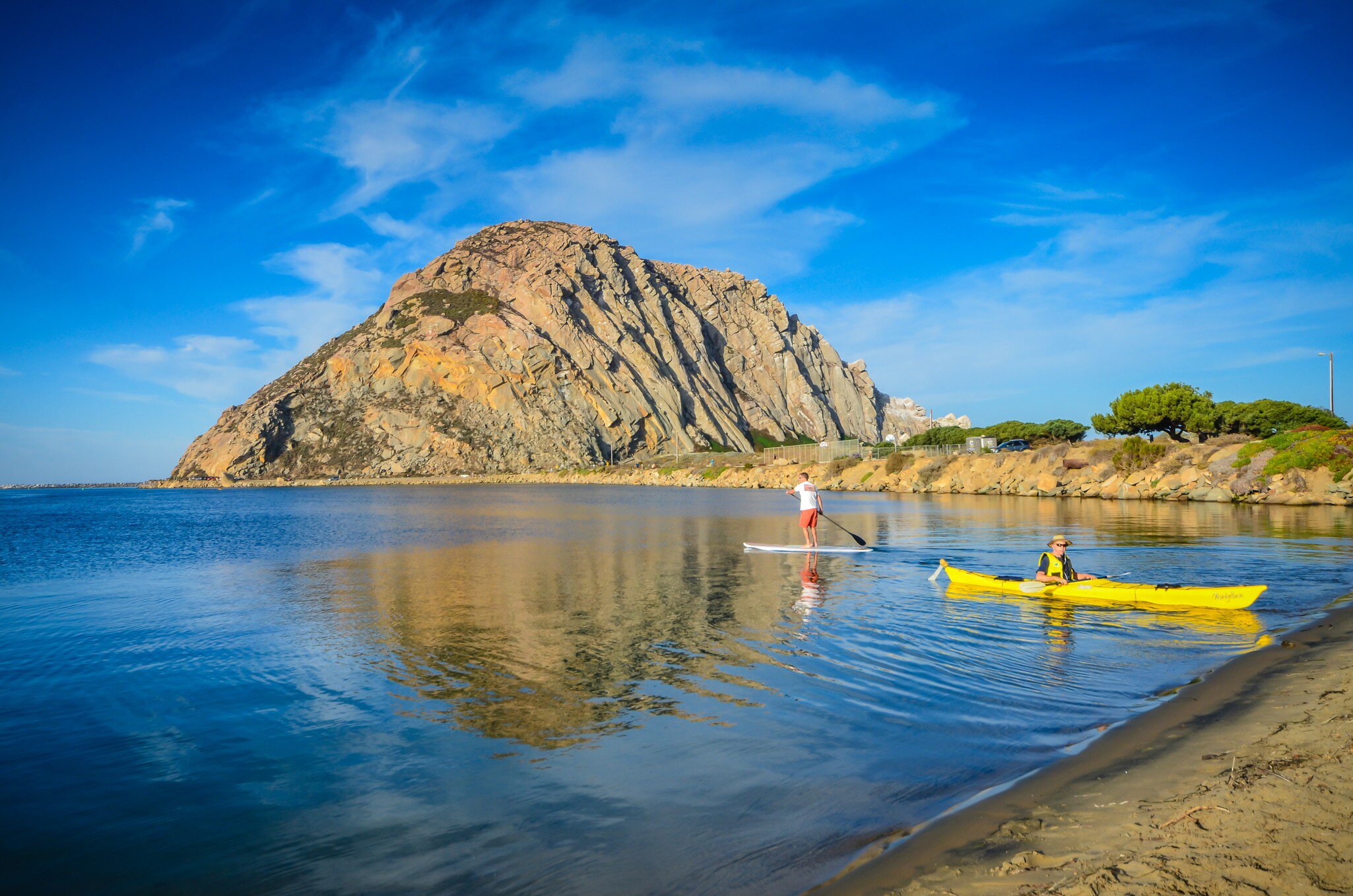 Kayaker and stand up paddleboarder head out on the calm waters of Morro Rock Harbor in Central California.