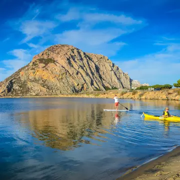 Kayaker and stand up paddleboarder head out on the calm waters of Morro Rock Harbor in Central California.