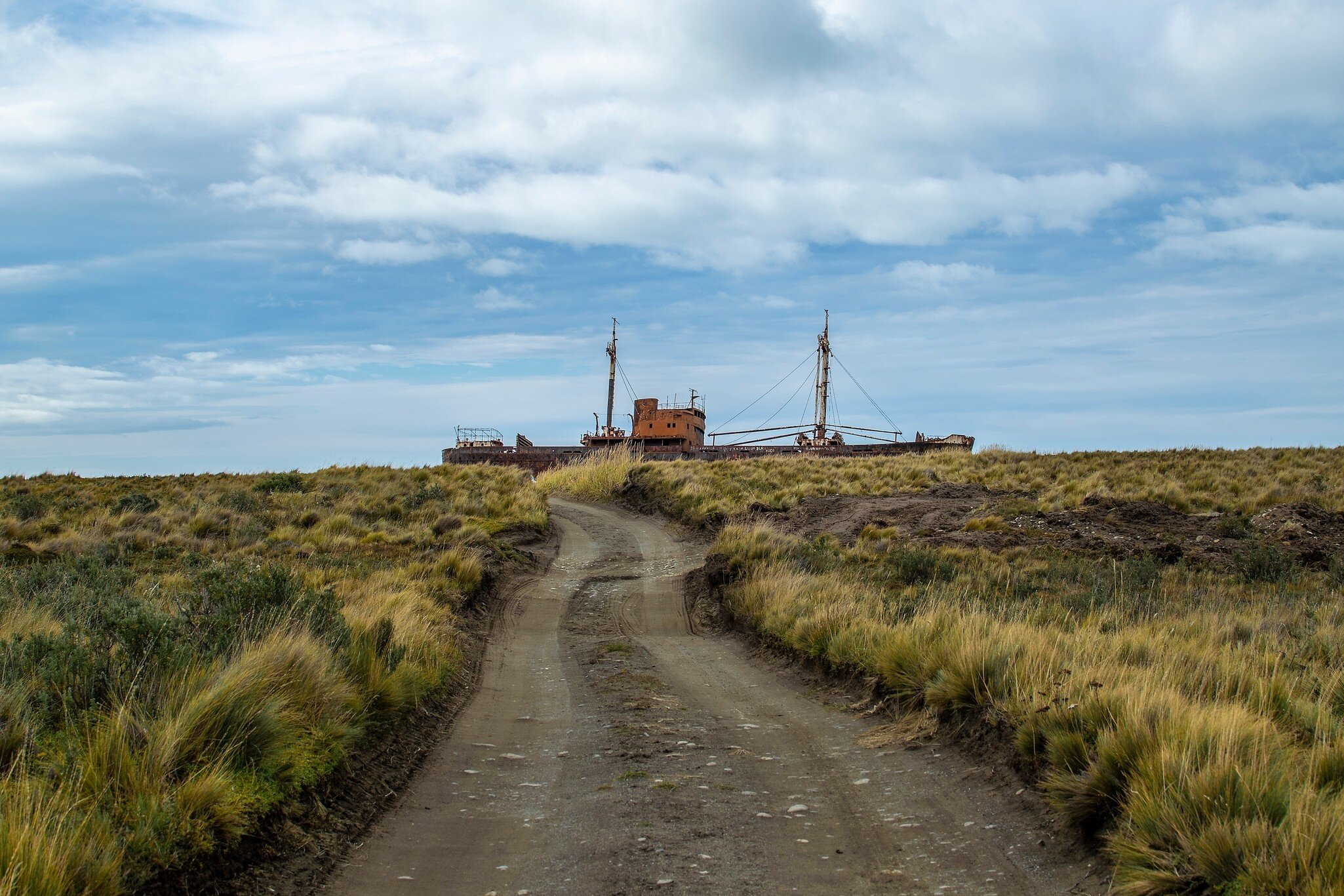 Dirt road and abandoned aground commercial ship at horizon in Cabo san Pablo, Tierra del Fuego, Argentina.