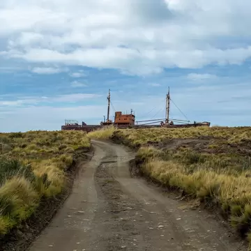 Dirt road and abandoned aground commercial ship at horizon in Cabo san Pablo, Tierra del Fuego, Argentina.