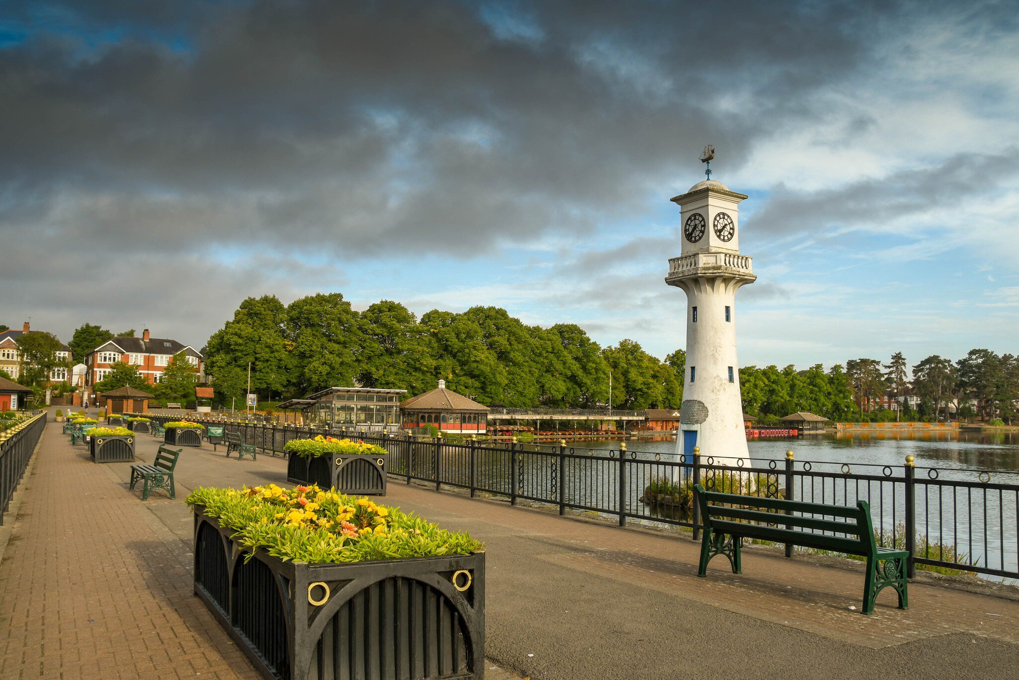 Wide angle view of the seats and flower boxes on the walkway alongside The Scott Memorial in Roath Park Lake in Cardiff. The sky has dark clouds. Cardiff, Wales.