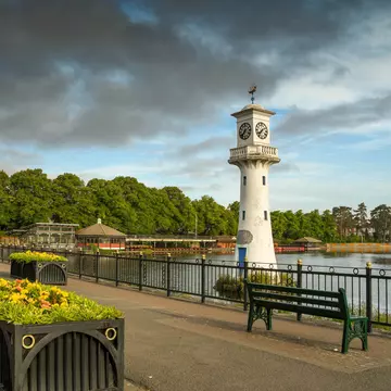 Wide angle view of the seats and flower boxes on the walkway alongside The Scott Memorial in Roath Park Lake in Cardiff. The sky has dark clouds. Cardiff, Wales.