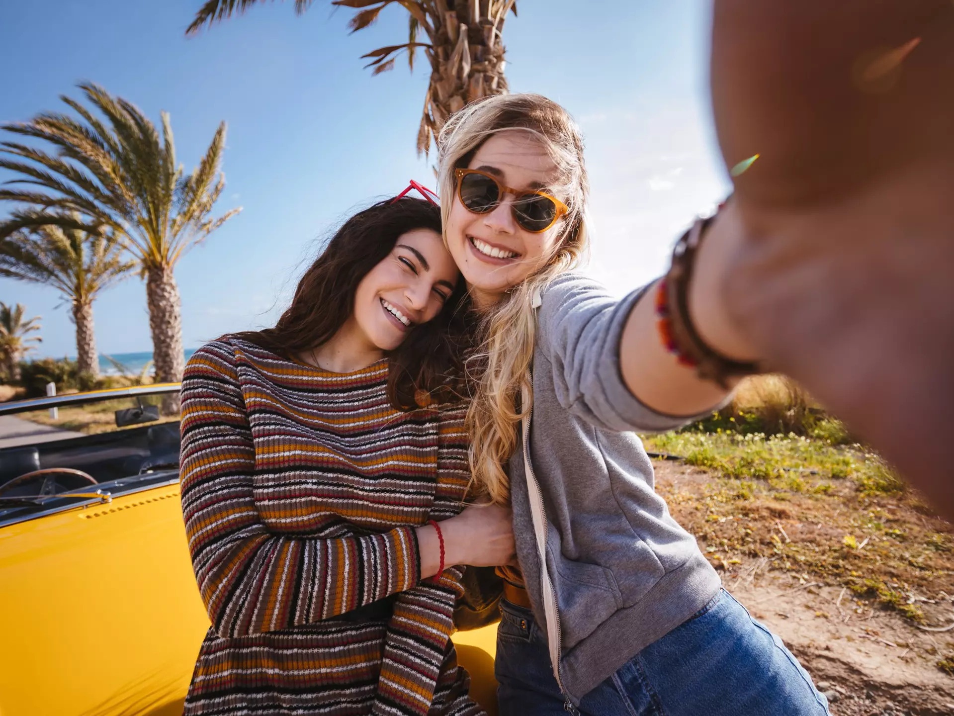 Two women pose in front of palm trees and a yellow car in Cyprus
964793310