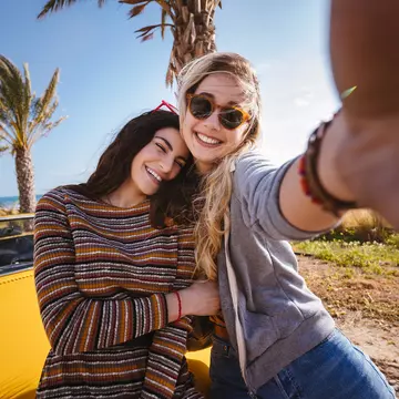 Two women pose in front of palm trees and a yellow car in Cyprus
964793310