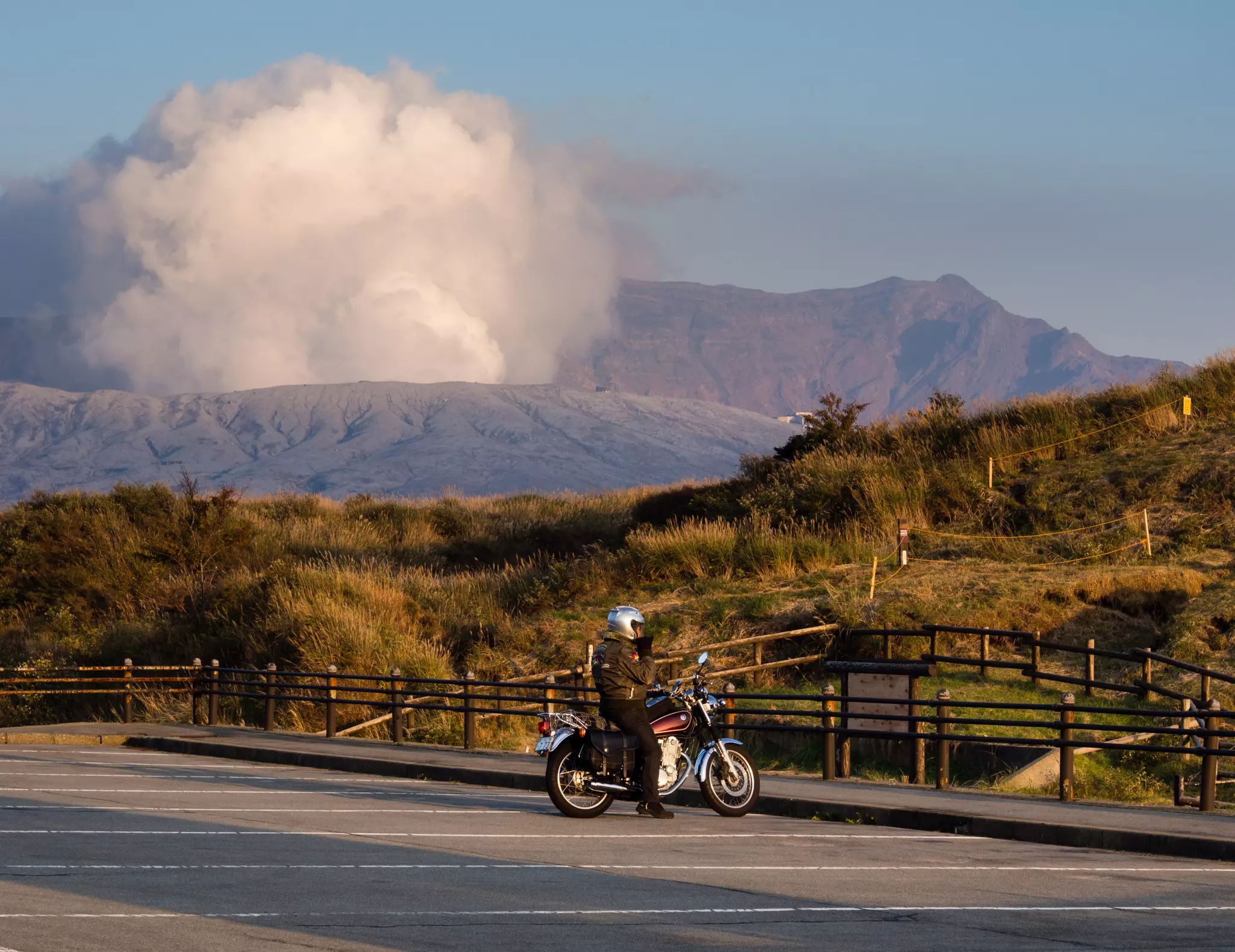 Biker stopped at a parking lot with fuming volcanic crater at the background