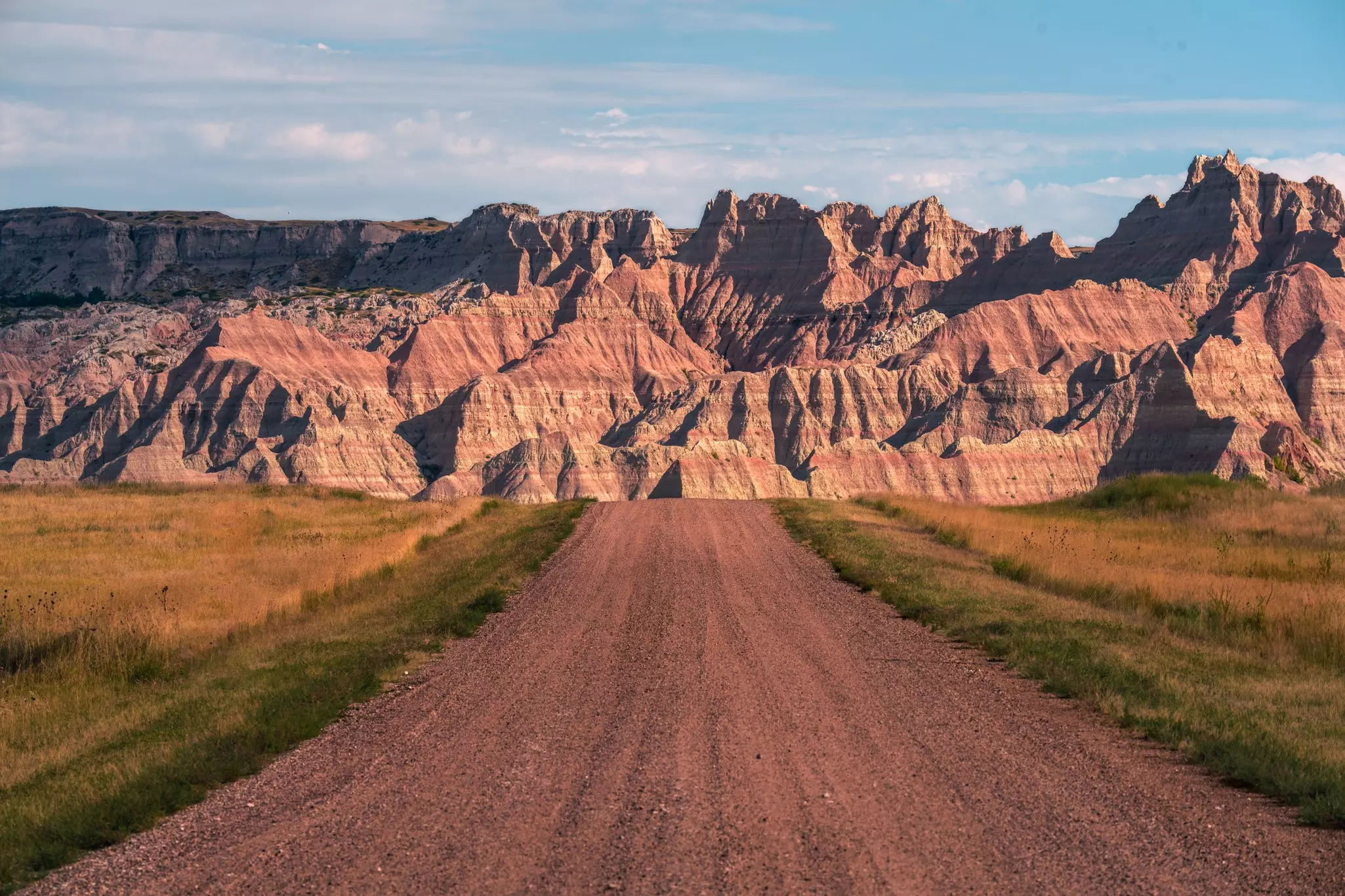 A dirt track through a national park heading towards huge red-rock escarpments.