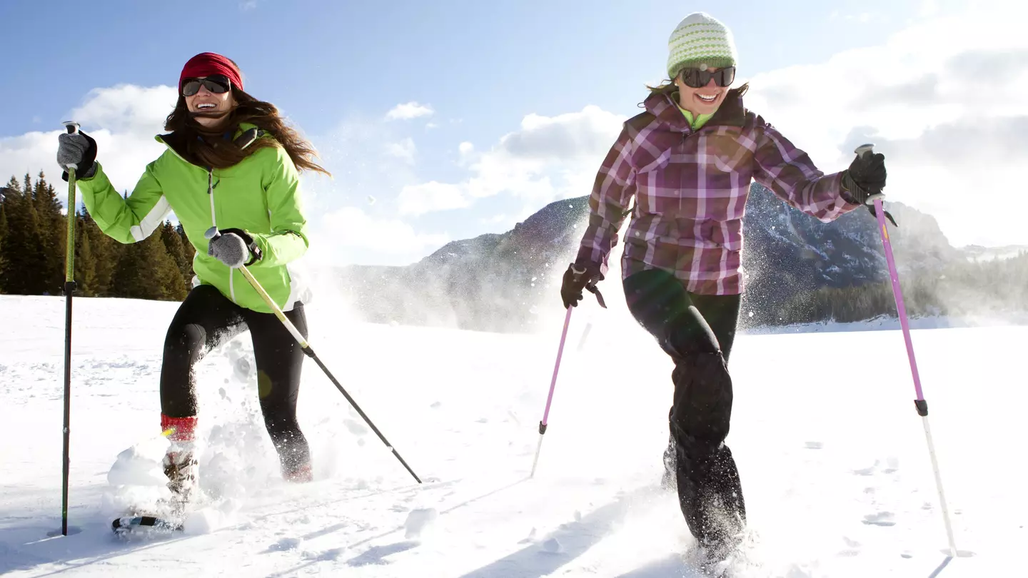 Two smiling women snowshoeing on a sunny winter day