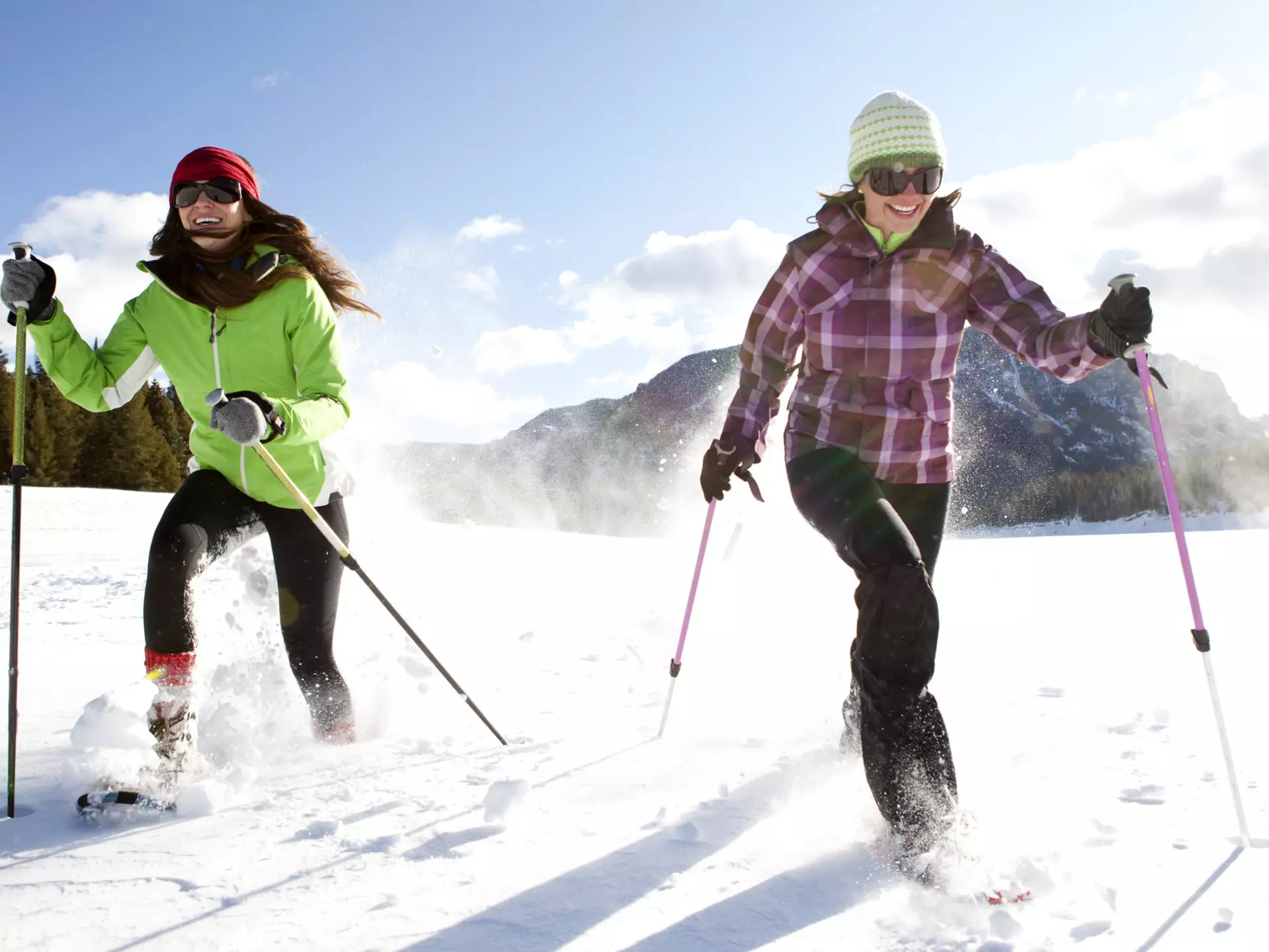 Two smiling women snowshoeing on a sunny winter day