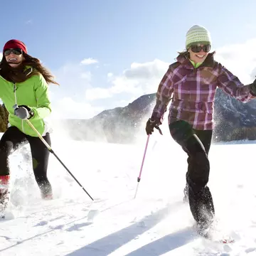 Two smiling women snowshoeing on a sunny winter day