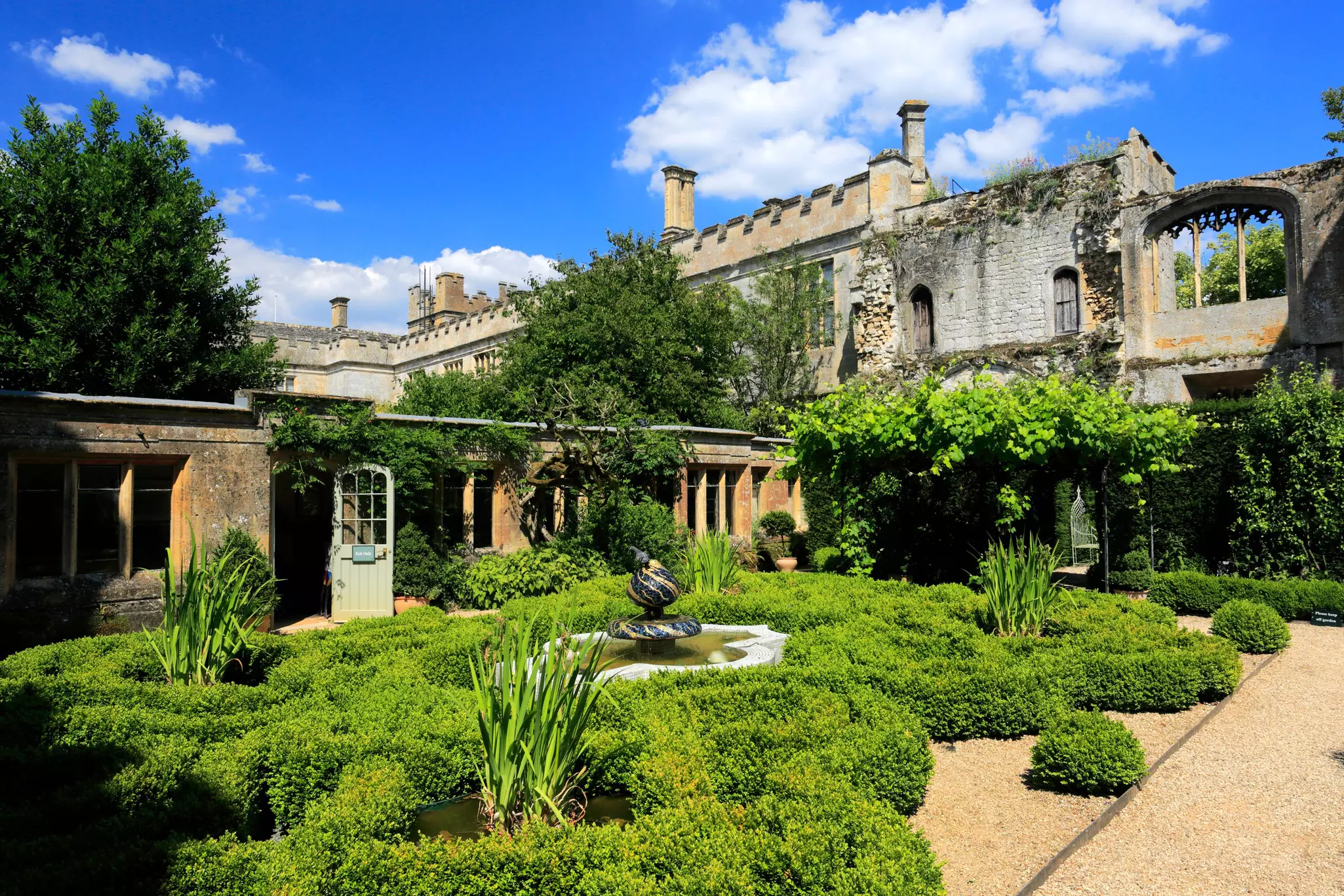 Greenery around a pond in a garden backed by a Tudor castle.