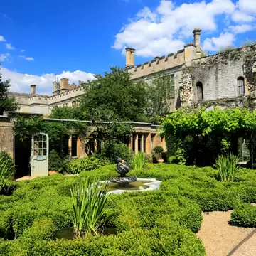 Greenery around a pond in a garden backed by a Tudor castle.