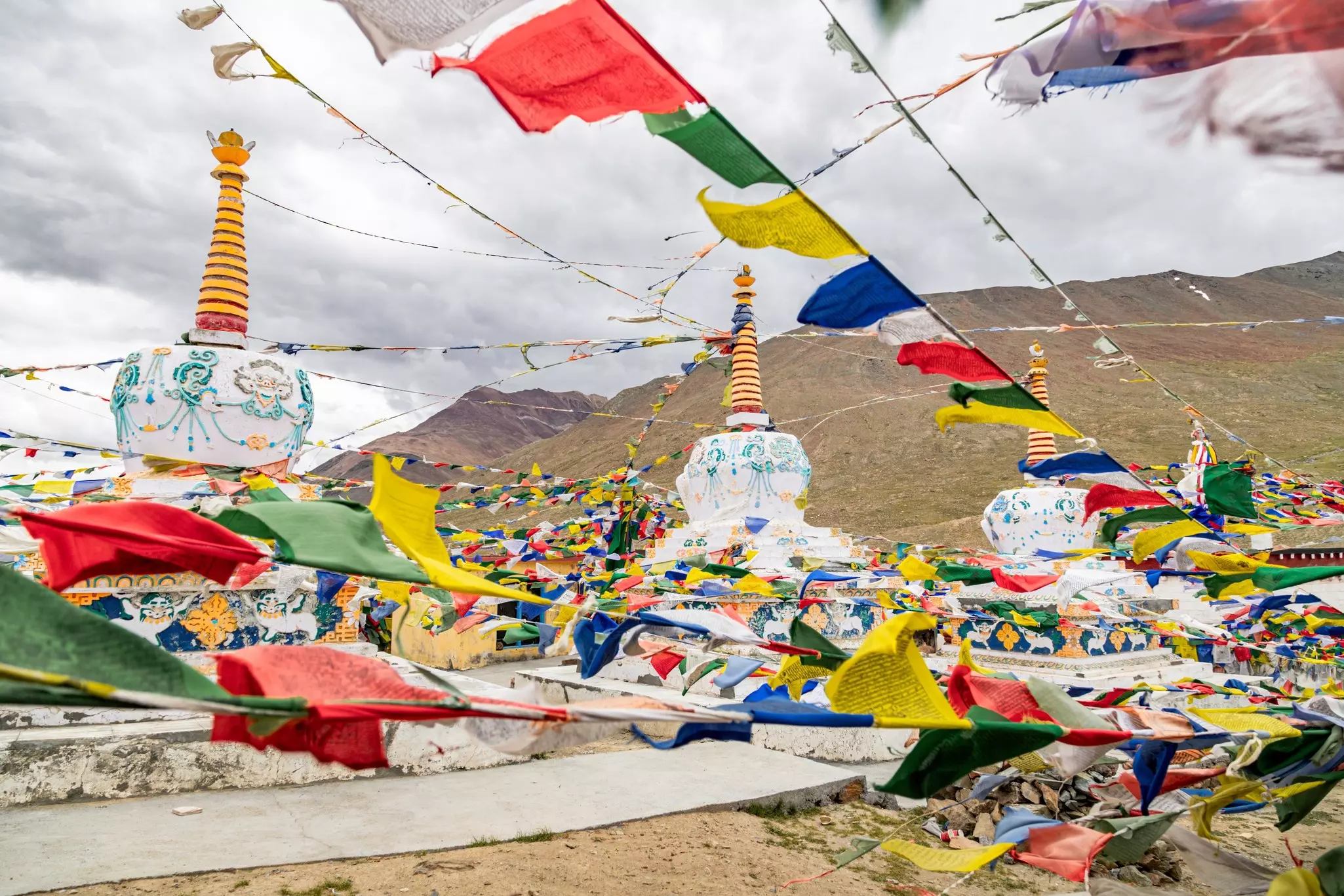 Brightly colored flags strung along ropes flutter next to stupas at a high pass in the mountains.