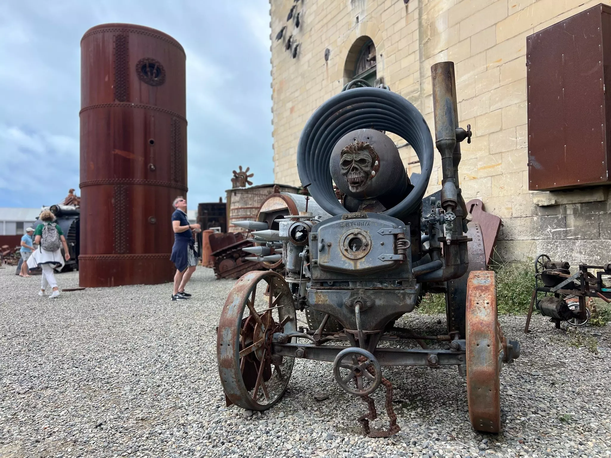 A rusting sculpture on wheels, made of old bits of machinery with a skull on the front. 