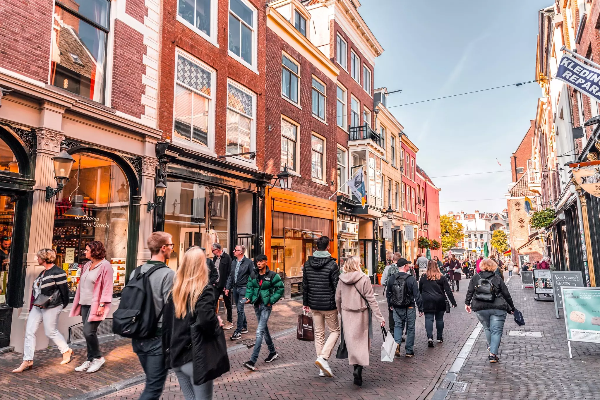 People walk down a pedestrianized street lined with shops in the center of a city.