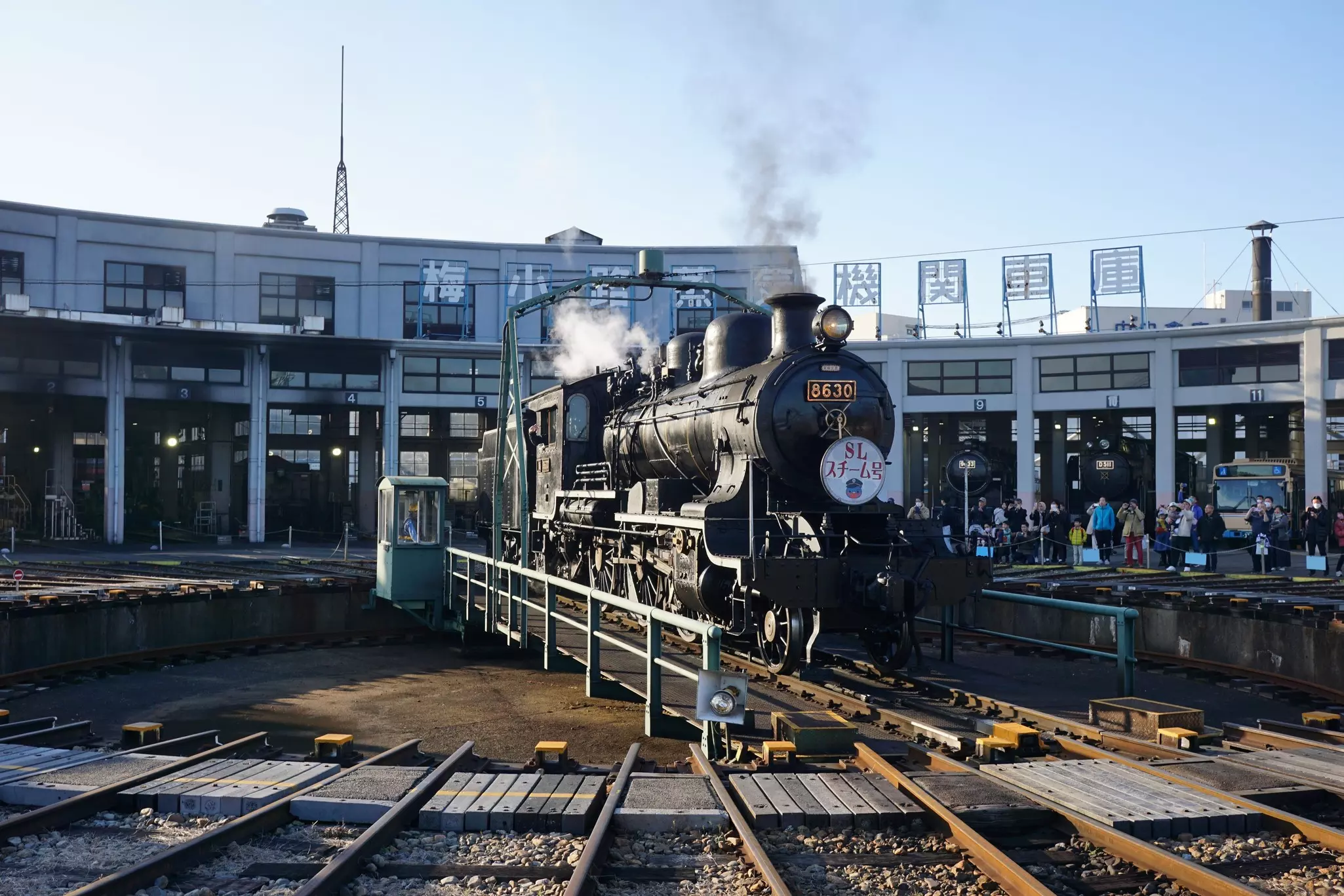 A historic steam locomotive is on display at a roundhouse as part of a museum exhibit.