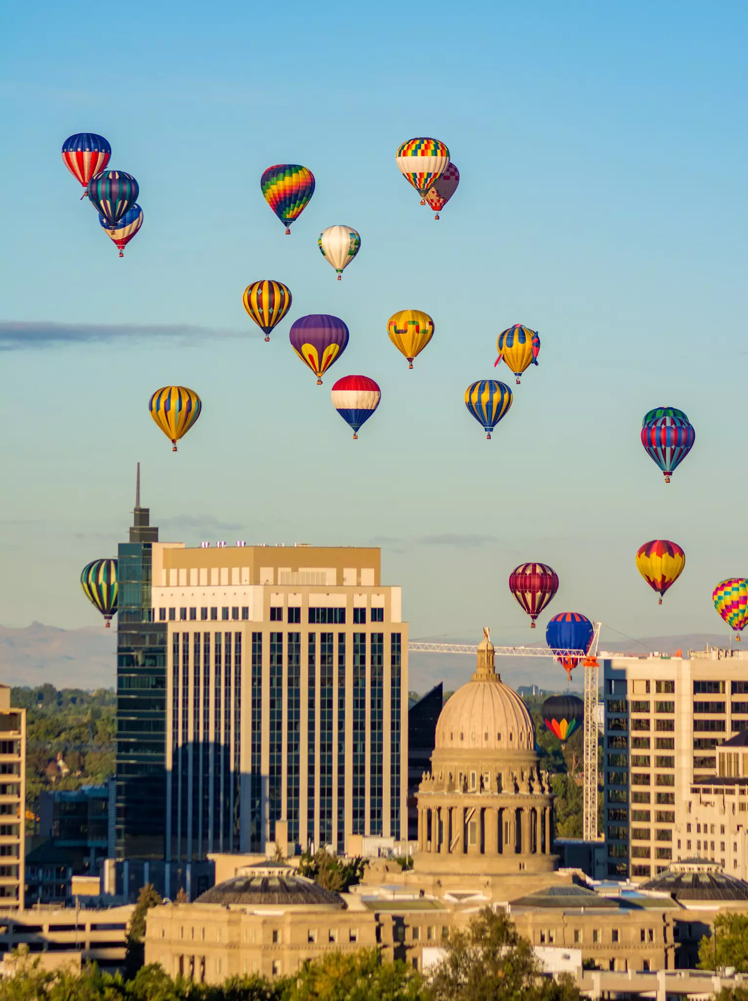 Seven hot air balloons in the sky over downtown buildings, including a domed capital.