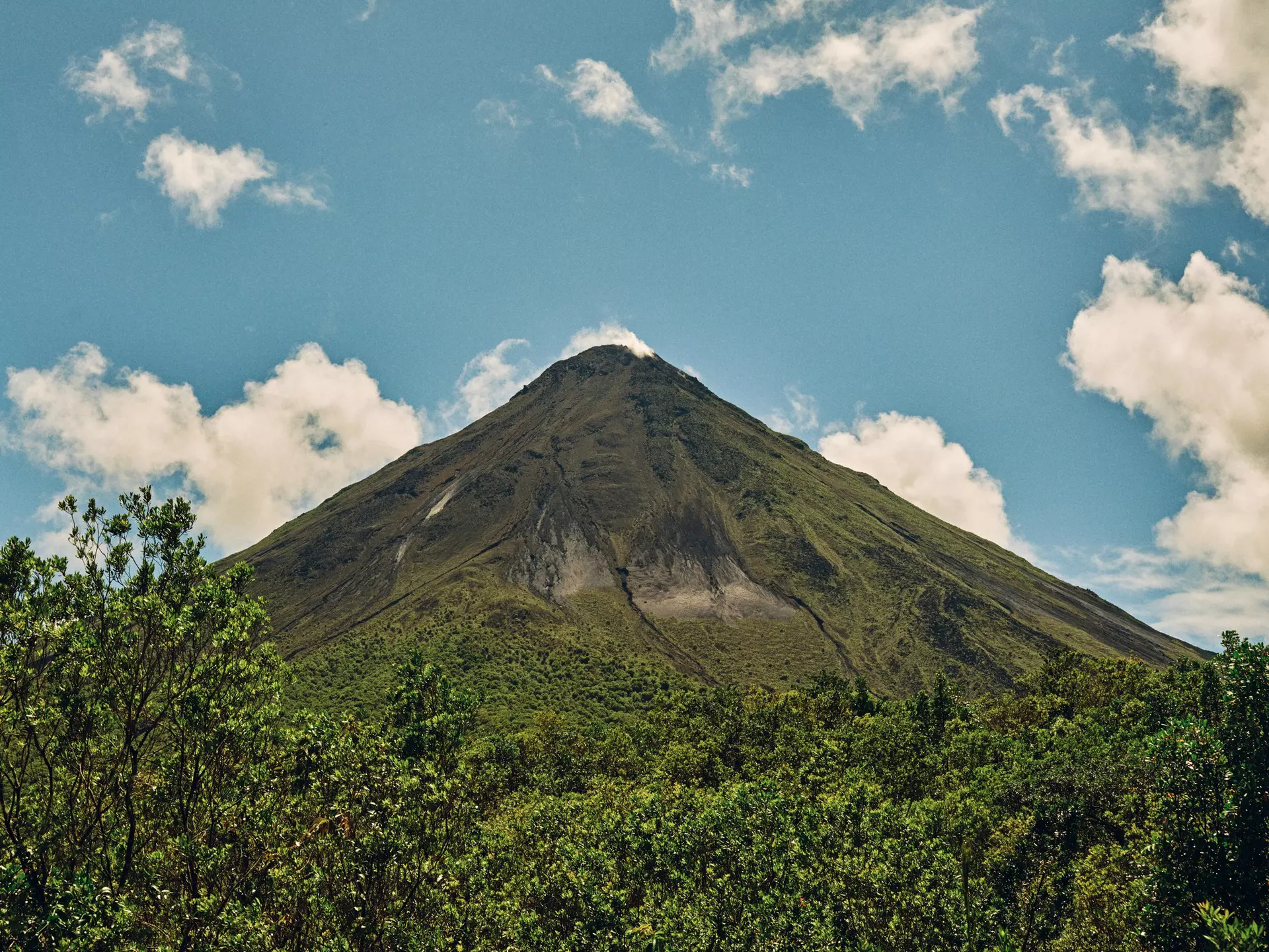 Close-up of a volcano surrounded by lush jungle on a blue-sky day