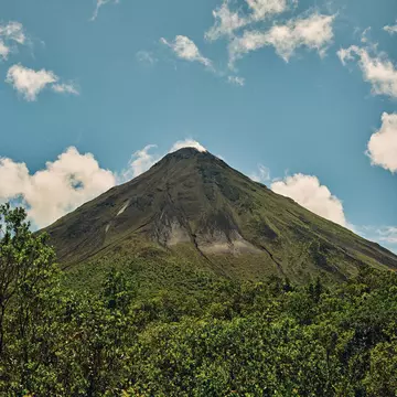 Close-up of a volcano surrounded by lush jungle on a blue-sky day