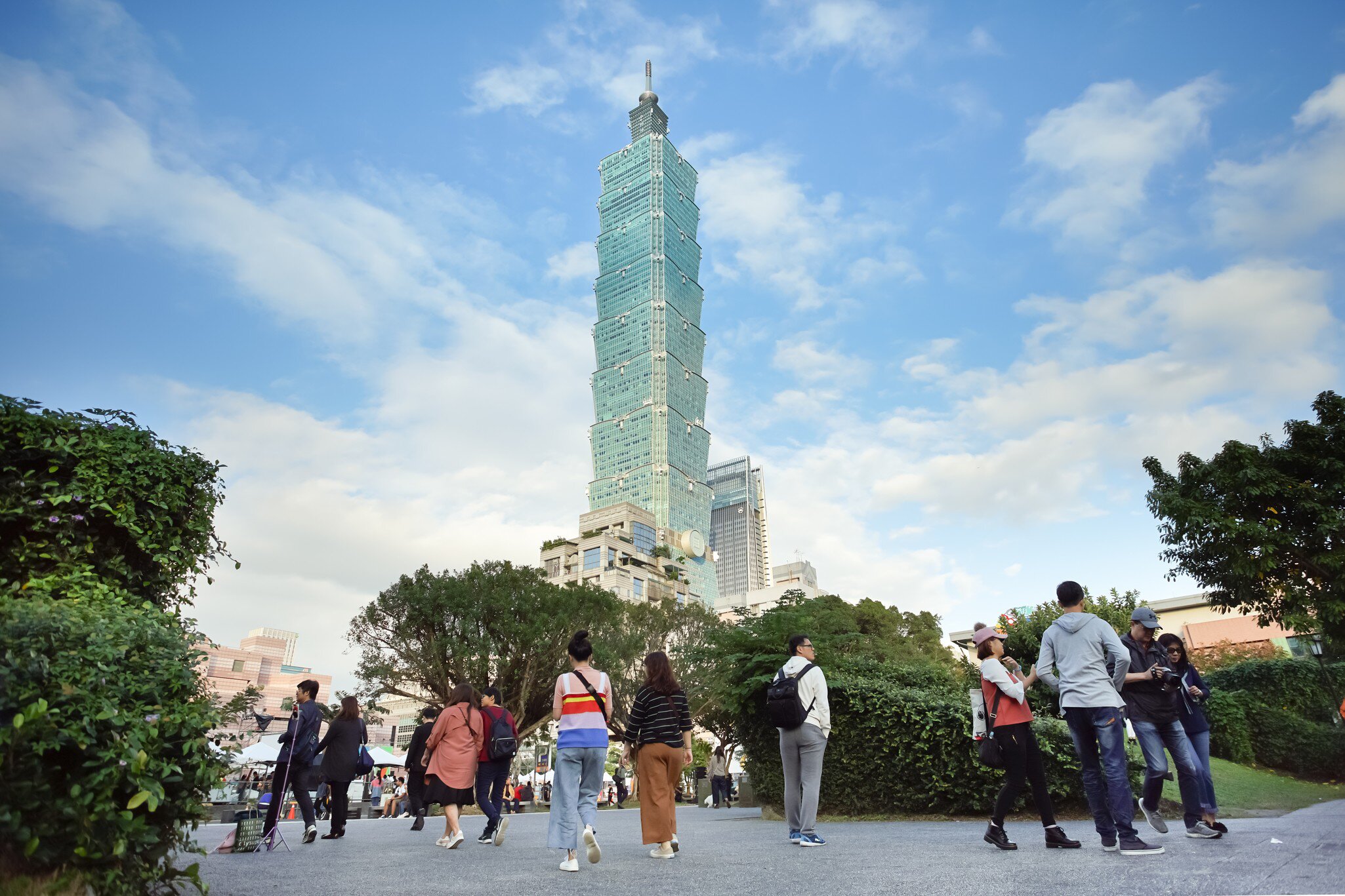 People walking around at the base of the light green Taipei 101 tower.