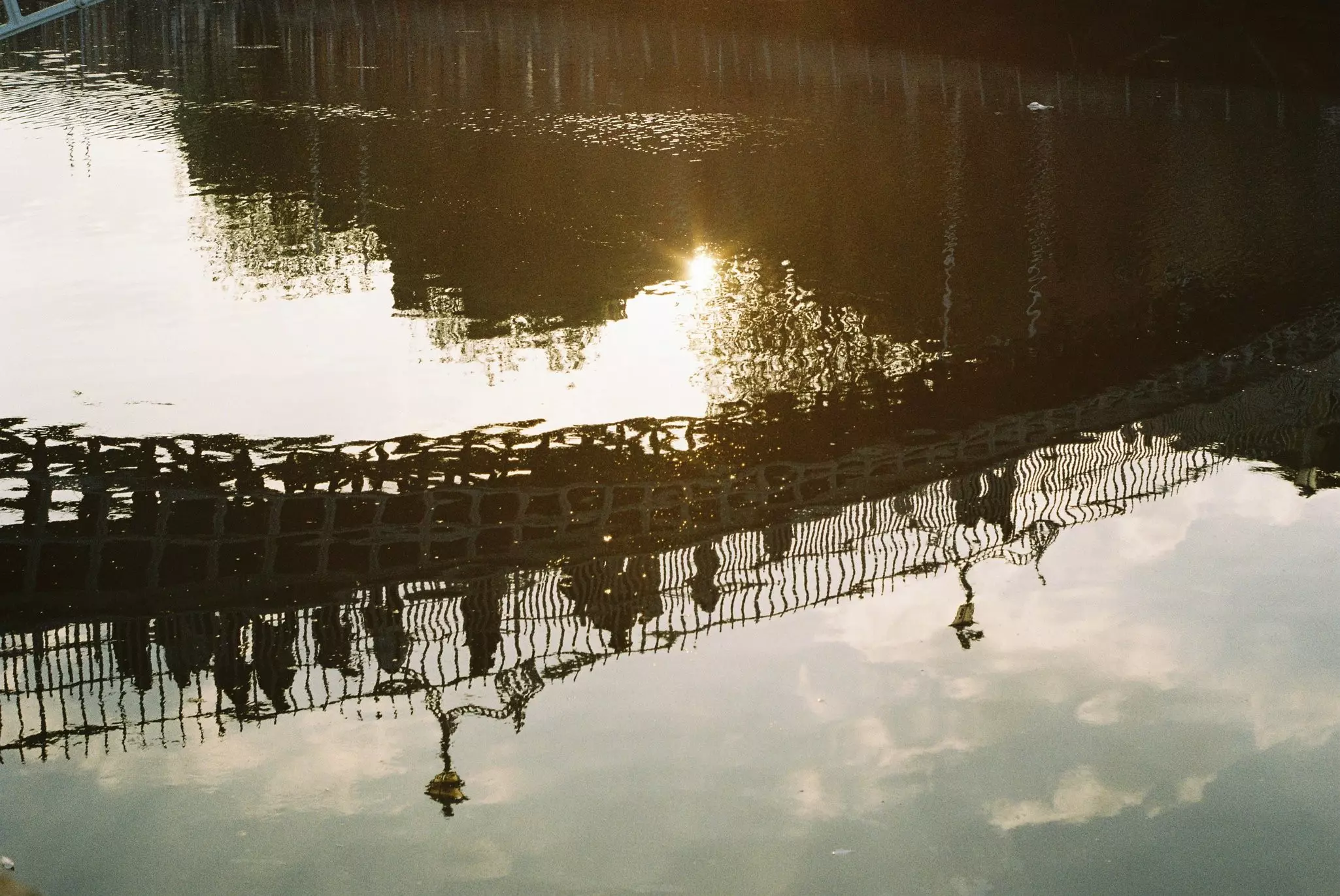 Reflection in a river of people walking on a bridge over the water.