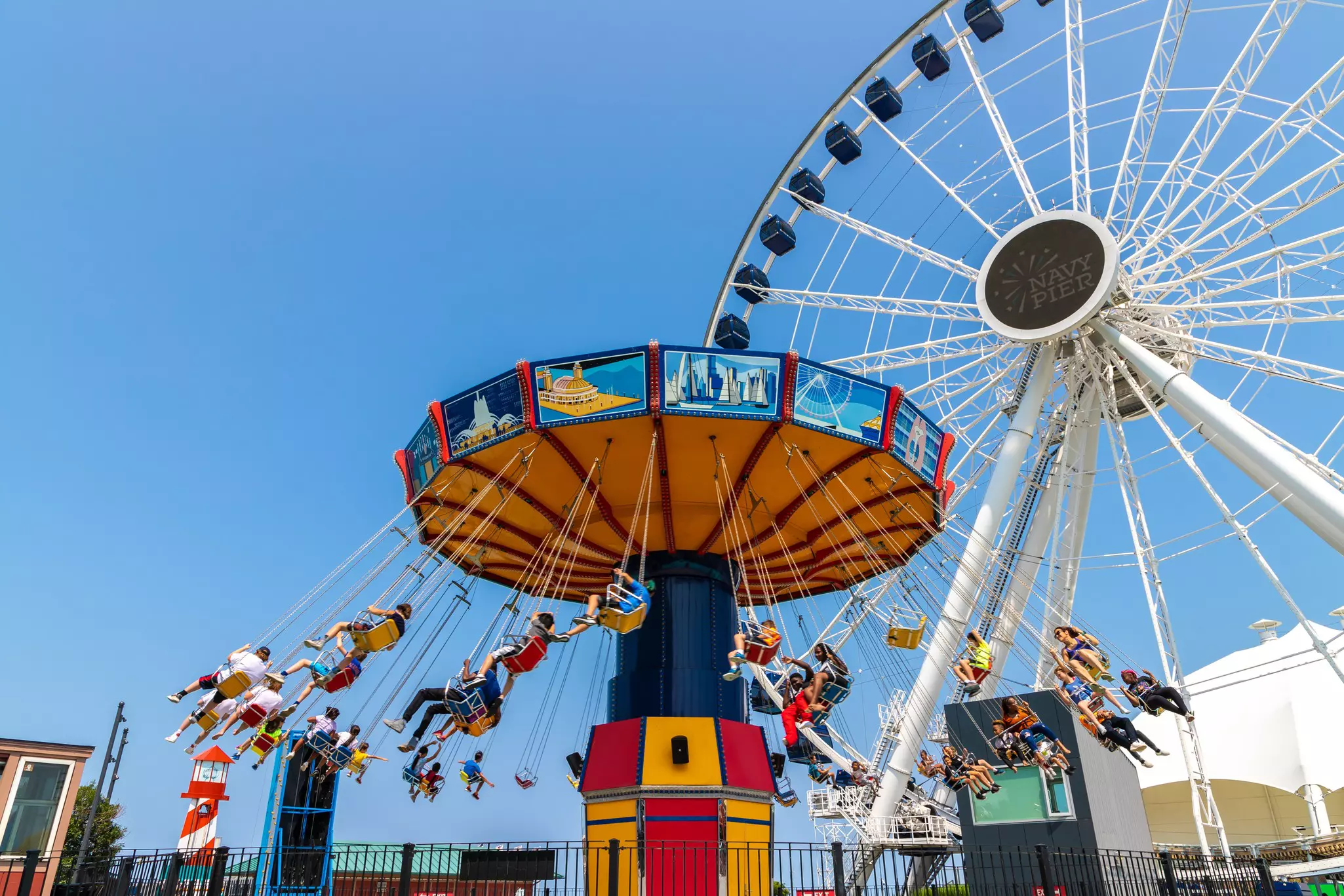 Large white ferris wheel with a swing carousel full of riders in the foreground