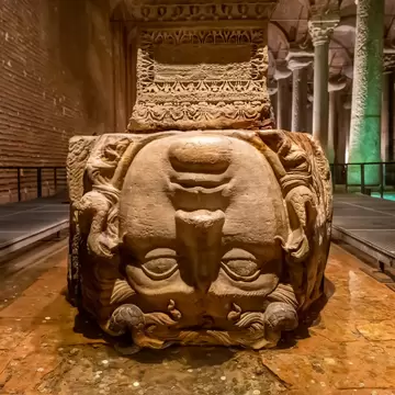 Carved stone Medusa head set upside down under a column in an Istanbul Byzantine cistern, coins on the floor, walkways beside