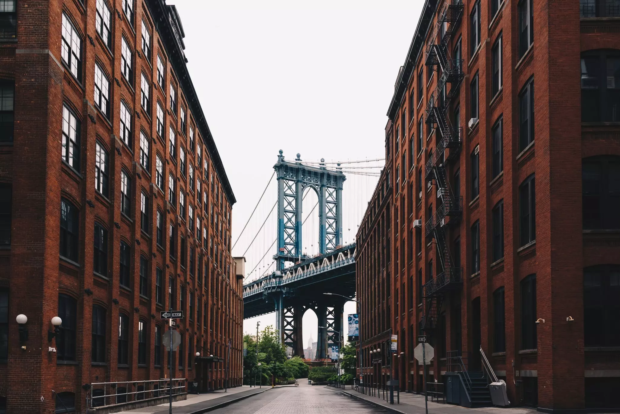 A large bridge at the end of a narrow street lined by tall red brick buildings.