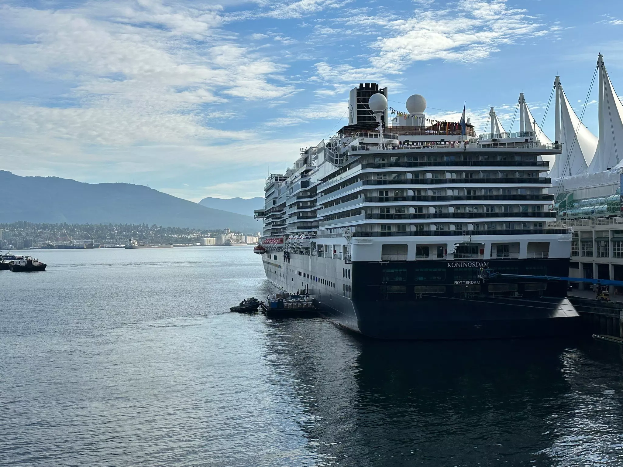 A cruise ship at port on a sunny day with low mountains in the distance.