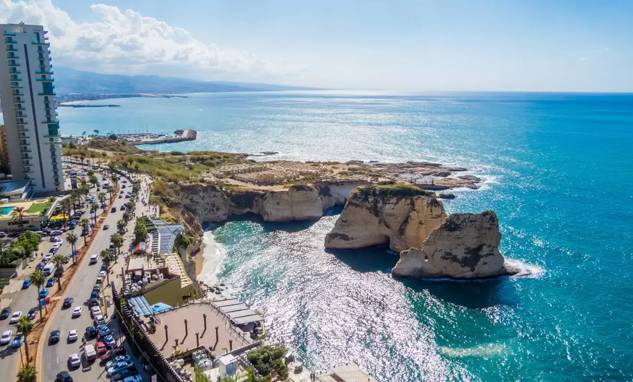 Aerial view of Pigeon Rocks sea stacks off Beirut's Raouché cliffs, with a busy coastal road and high-rise on the left