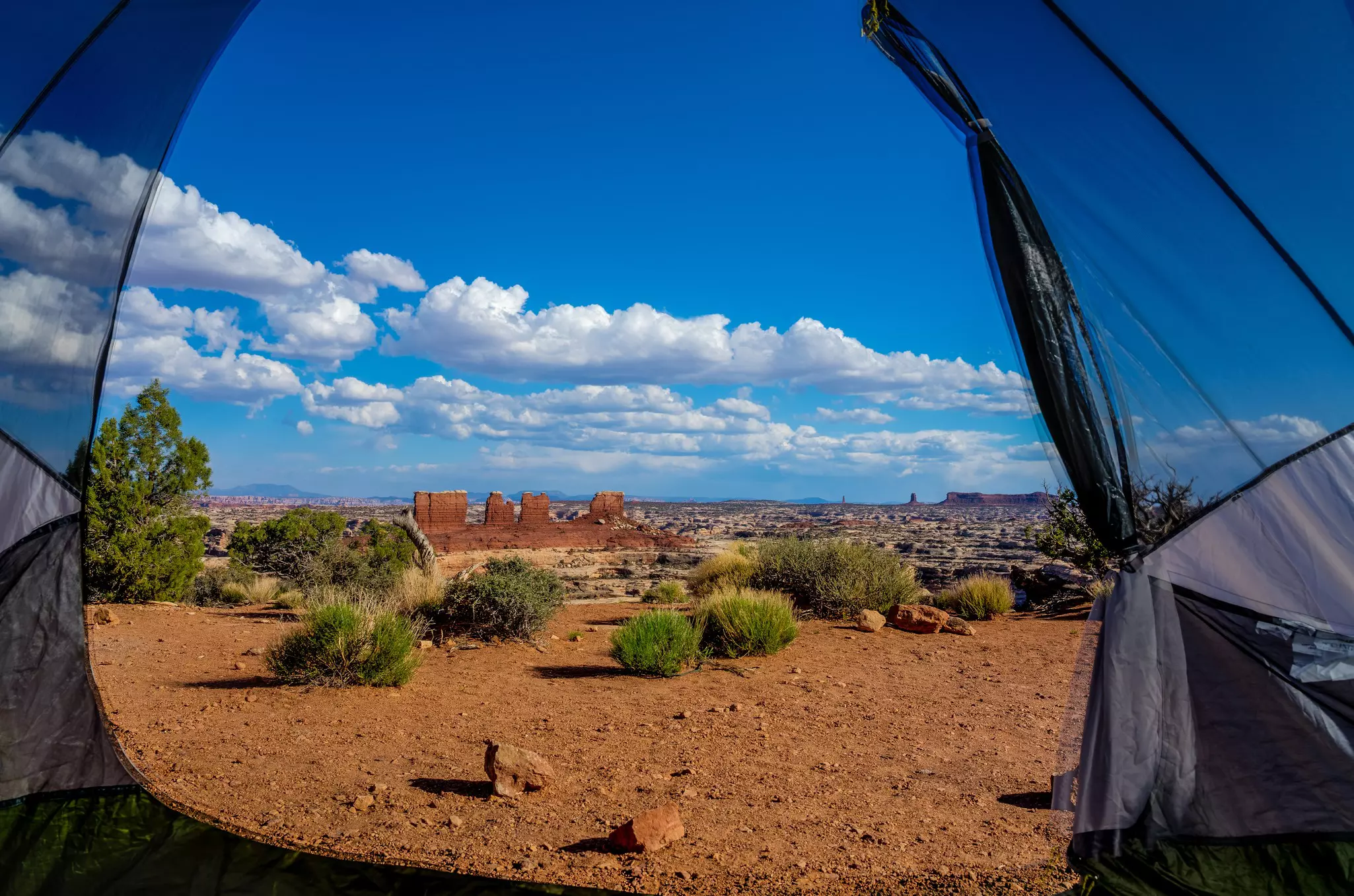 Looking out from inside a tent at a scrub-brush desert and red rock formations in the distance at The Maze Overlook in Canyonlands National Park.