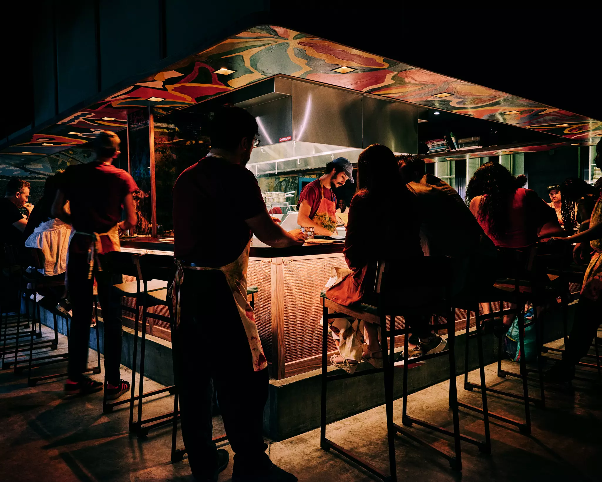 Diners sit on stools at a bar around an open kitchen at Kabawa in the East Village, New York City.