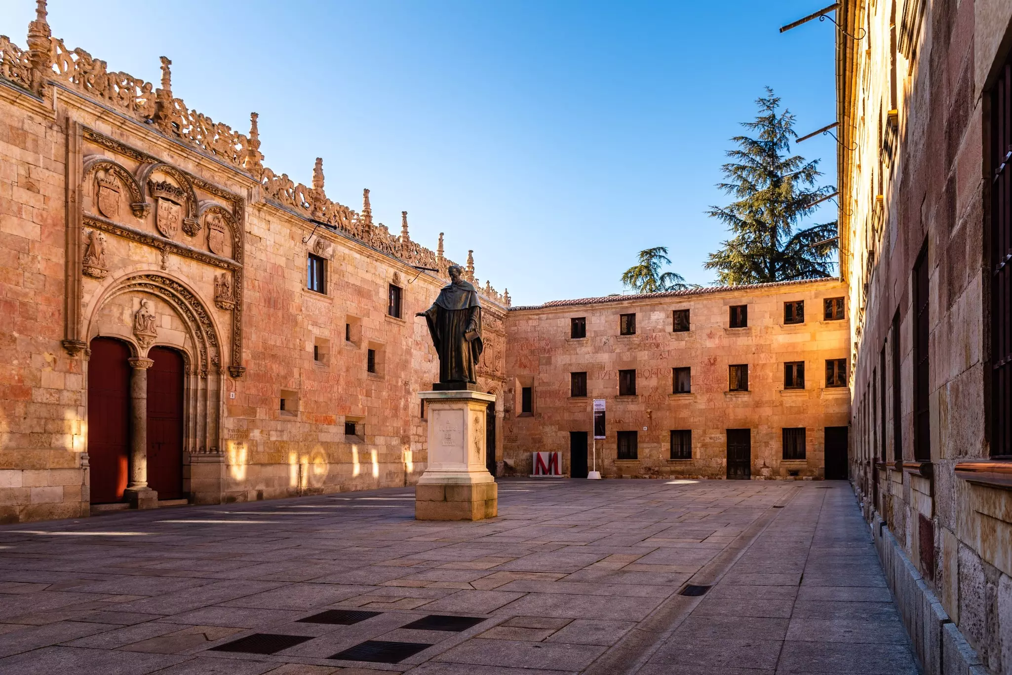Fray Luis de Leon statue in a square of the University of Salamanca with a blue sky above.