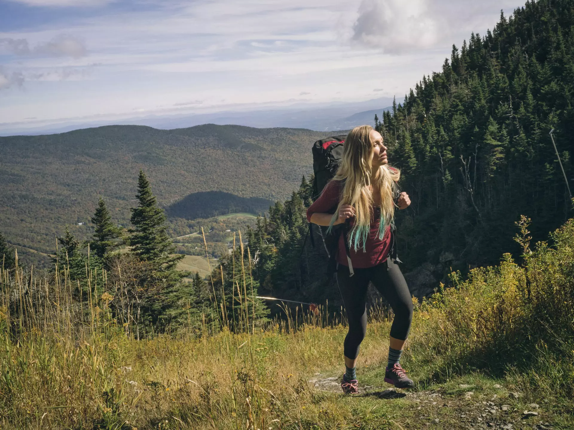 A woman wearing a large backpack hikes on a grassy trail at Mount Mansfield in Vermont