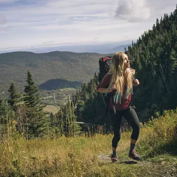 A woman wearing a large backpack hikes on a grassy trail at Mount Mansfield in Vermont