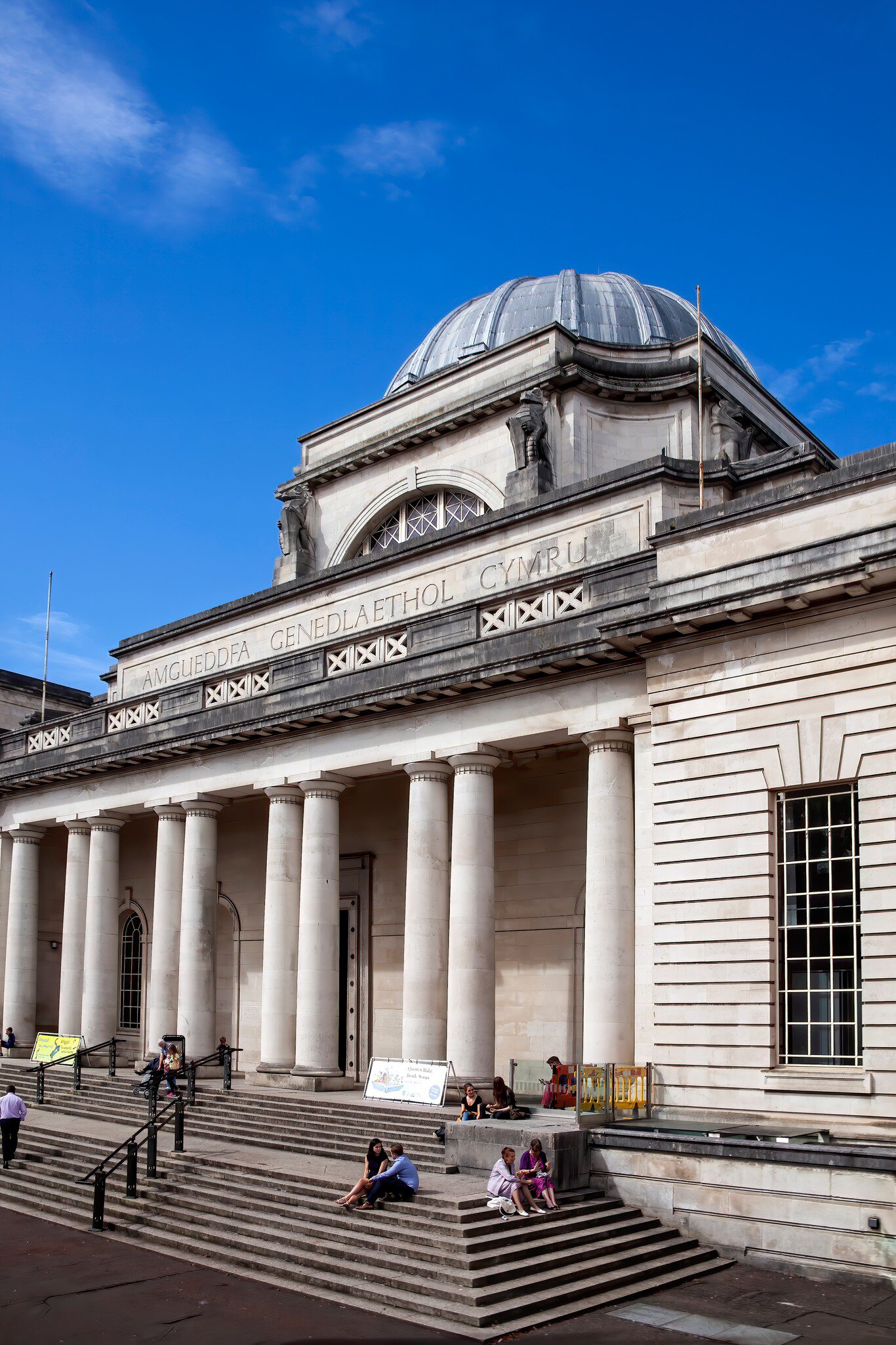 People sitting on the steps of the National Museum and art gallery which is a popular travel destination tourist attraction landmark of the city in Cardiff, Wales.