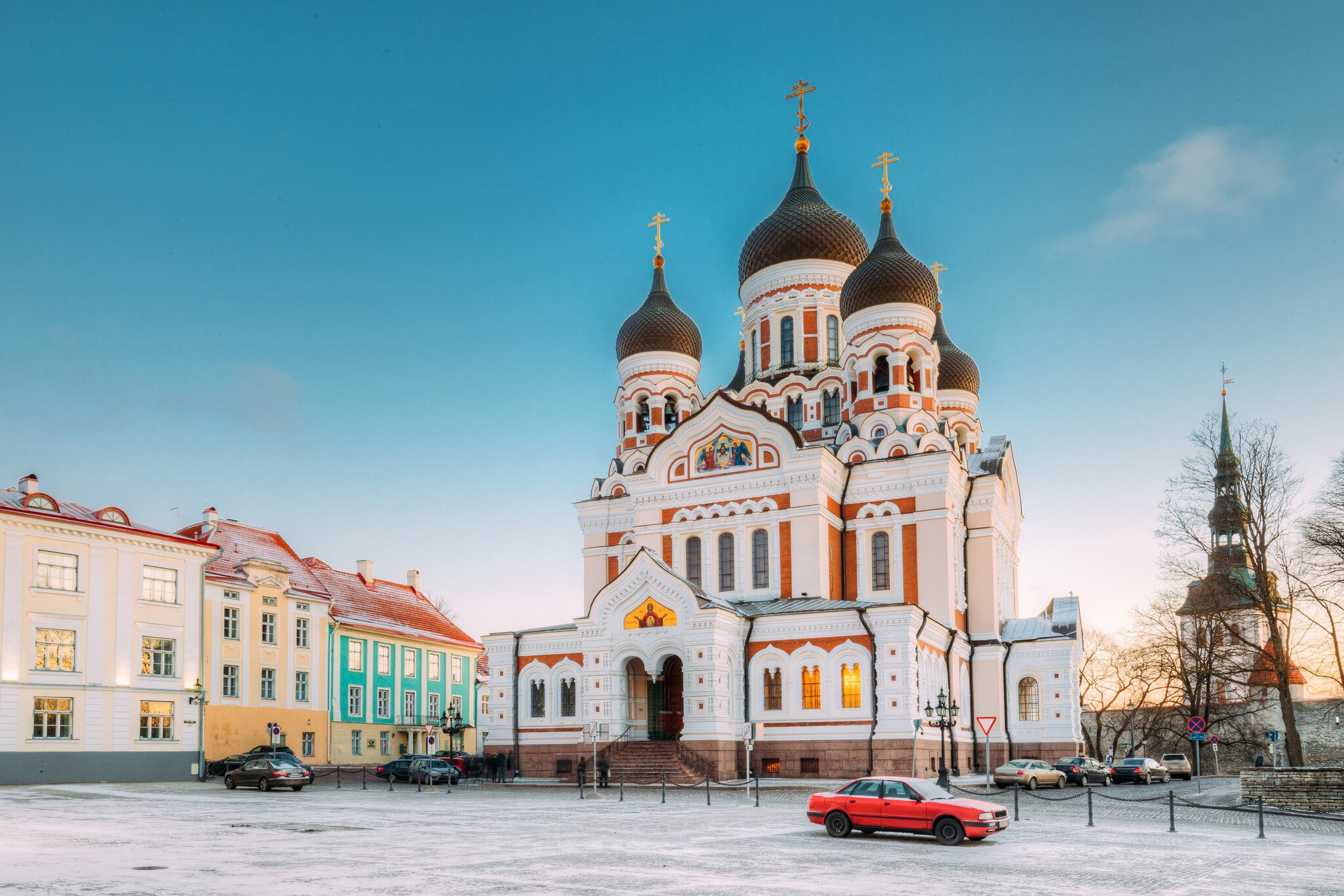 A white and orange Orthodox cathedral with black onion domes on a snowy square.