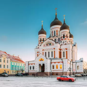 A white and orange Orthodox cathedral with black onion domes on a snowy square.