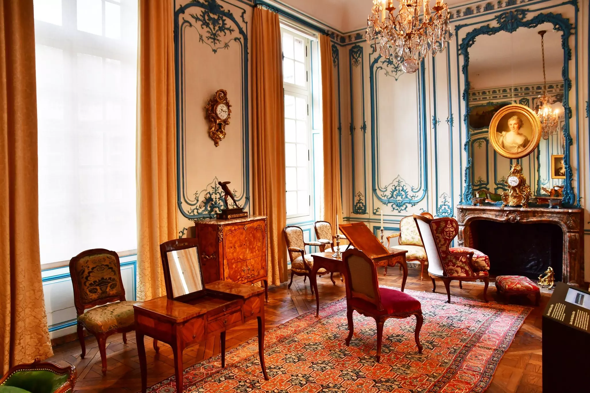 A furnished historical room in the Musee Carnavalet in Paris, featuring velvet chairs, a marble fireplace and ornate furniture pieces.