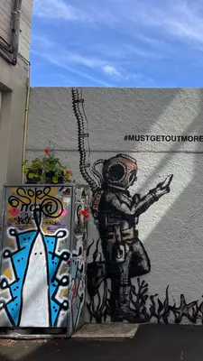 A street mural on a wall of an underwater diver in old-fashioned gear playing on a cell phone with a note that says "must get out more"