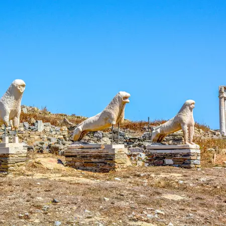 An ancient statue of a lion on a platform with a blue sky in the background. 
